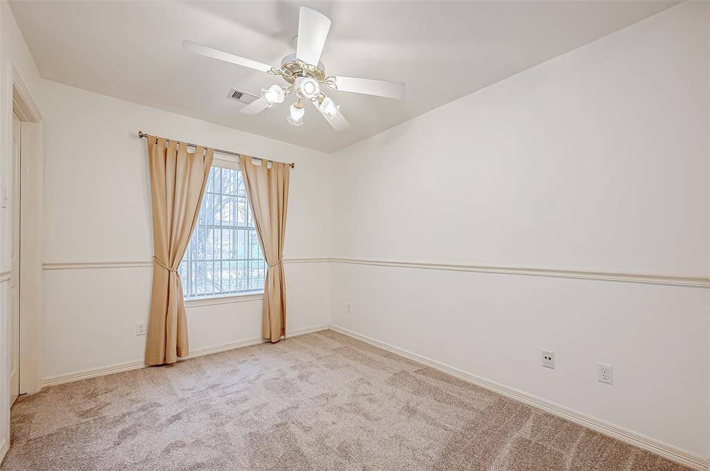 With warm-toned carpeting and a spacious layout, this bedroom offers a relaxing setting. The large window allows sunlight to brighten the space, while the ceiling fan provides airflow.