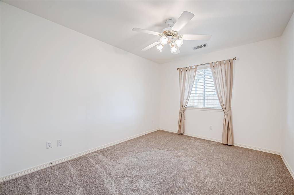A second well-sized bedroom mirrors the soft, neutral tones of the home, with plush carpeting and a ceiling fan for added comfort. The window enhances the sense of openness.