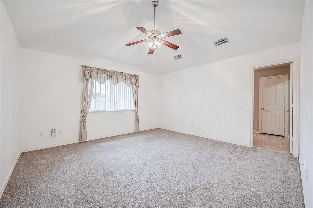 This expansive primary bedroom enjoys abundant natural light from a well-placed window, highlighting the crisp white walls and plush carpeting. A ceiling fan enhances comfort, while the en suite bath adds convenience.
