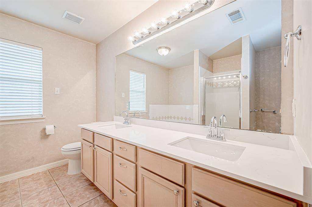 A blend of elegance and practicality, this en suite bathroom features a spacious dual vanity with abundant counter space and under-cabinet storage. The large mirror is framed by stylish lighting fixtures.