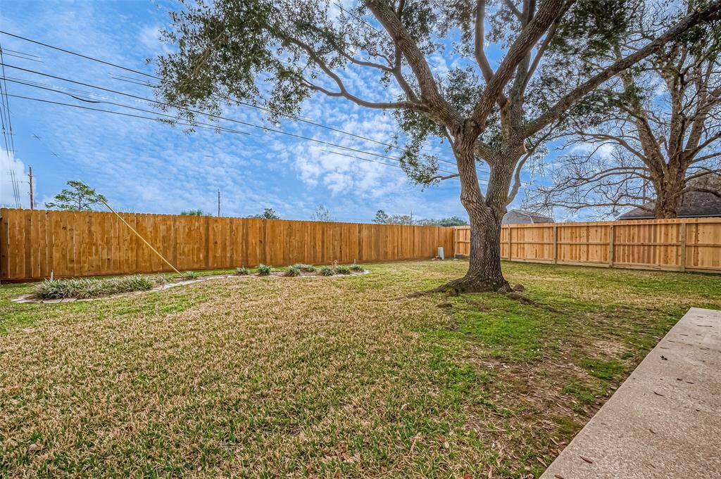 A sturdy wooden fence encloses the sprawling backyard, ensuring privacy while framing the lush green lawn. A mature tree adds shade and character to the space.