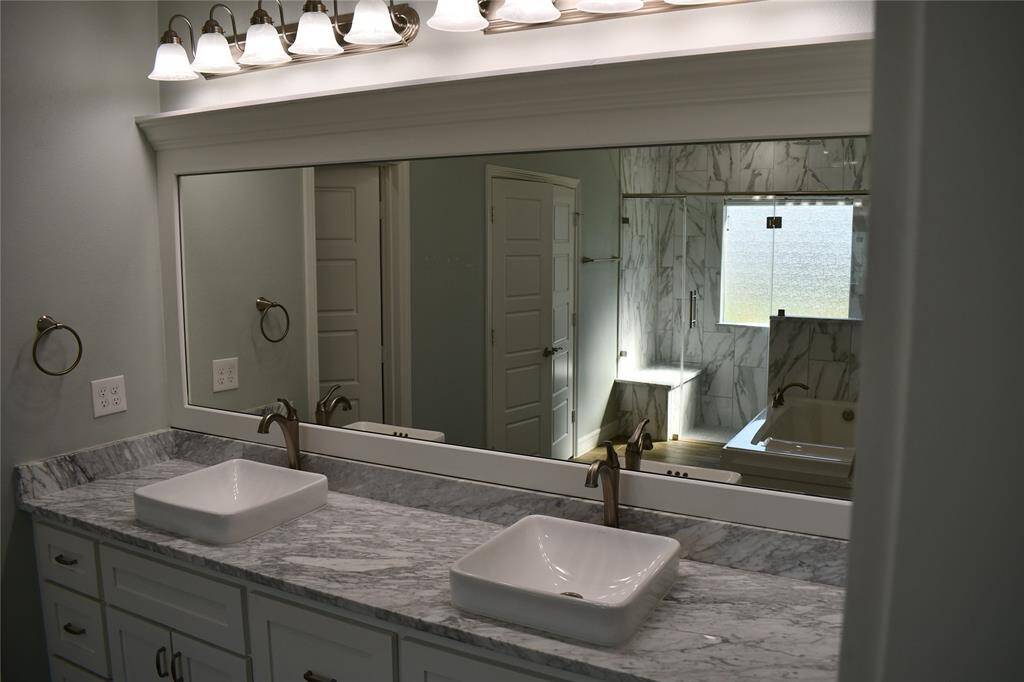 A well-lit en-suite bathroom; featuring a double sink, ample cabinetry for storage, and elegant marble sourced from Greece.