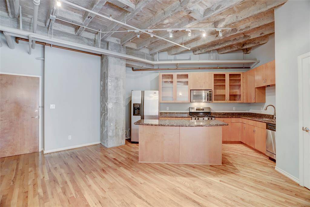 In this wider view of the kitchen, you can see the full layout, including the island that’s ideal for cooking and entertaining. To the left, you’ll notice the main door to the unit, conveniently located for easy access as you step into this inviting and functional space.