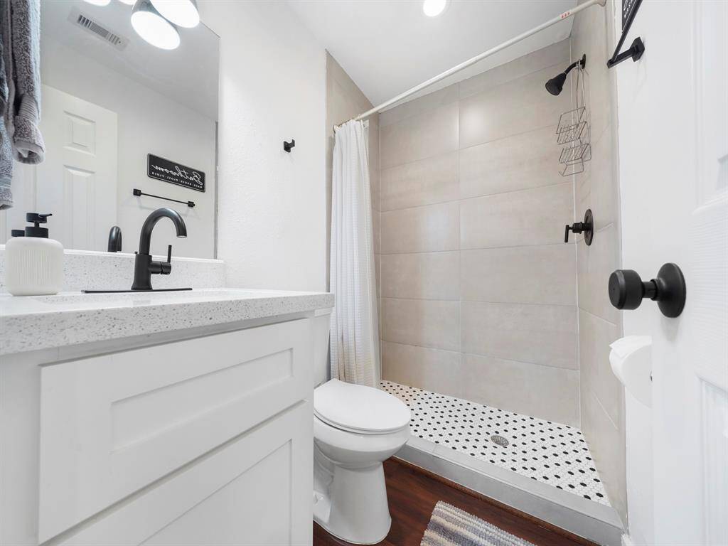Primary en-suite bathroom with large walk-in shower with floor to ceiling tile, quartz countertops and modern black fixtures.