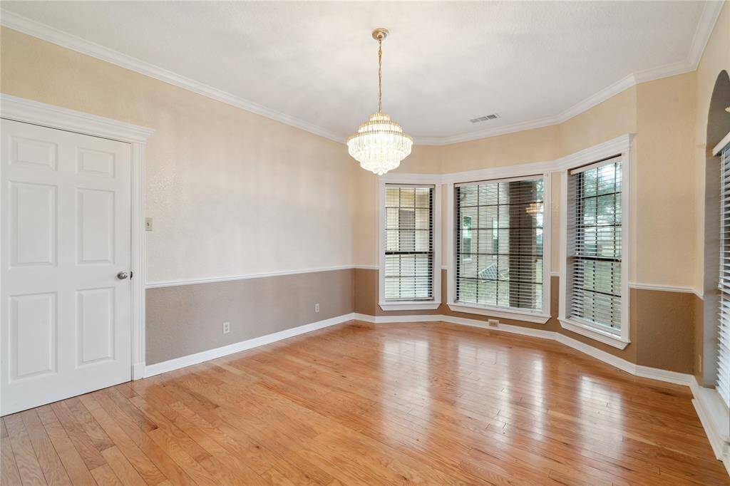 This dining room has hardwood flooring, a large bay window with blinds, and a chandelier, creating a bright and elegant space perfect for dining or entertaining.