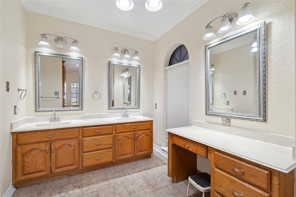 Primary bathroom features dual sinks with polished countertops, ample wooden cabinetry, and elegant framed mirrors. Vanity area and is well-lit with modern light fixtures, offering a bright and functional space.