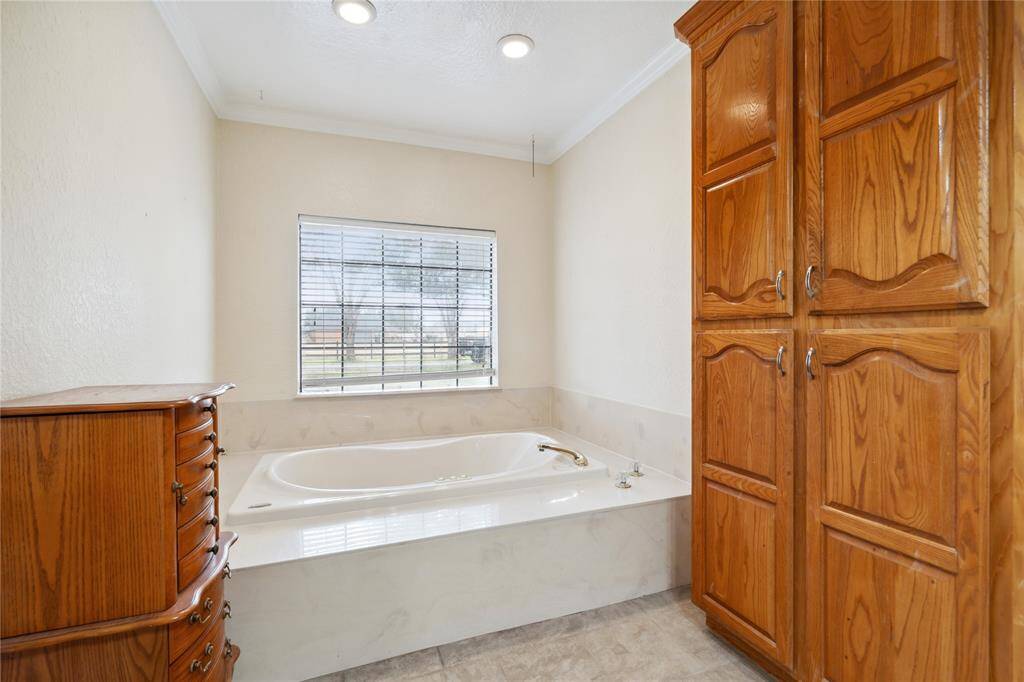 This bathroom features a relaxing built-in bathtub with a window view, complemented by ample wooden cabinetry for storage.