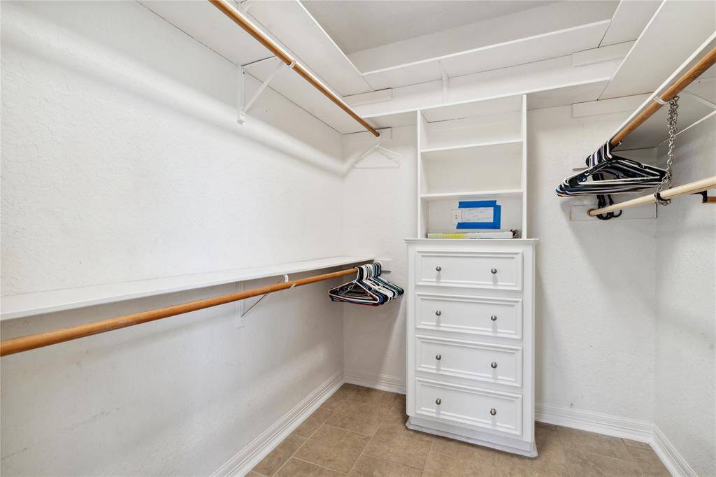 Spacious walk-in closet with ample hanging space and shelving. Features a built-in white dresser and neutral tile flooring, ideal for organizing clothing and accessories.
