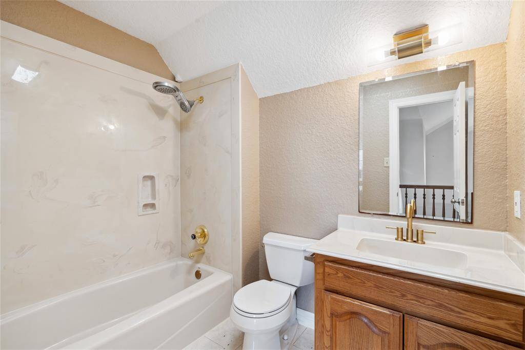 This bathroom features a bathtub with a shower, a toilet, and a vanity with a mirror. It has a warm, neutral color palette and modern lighting, creating a cozy and functional space.