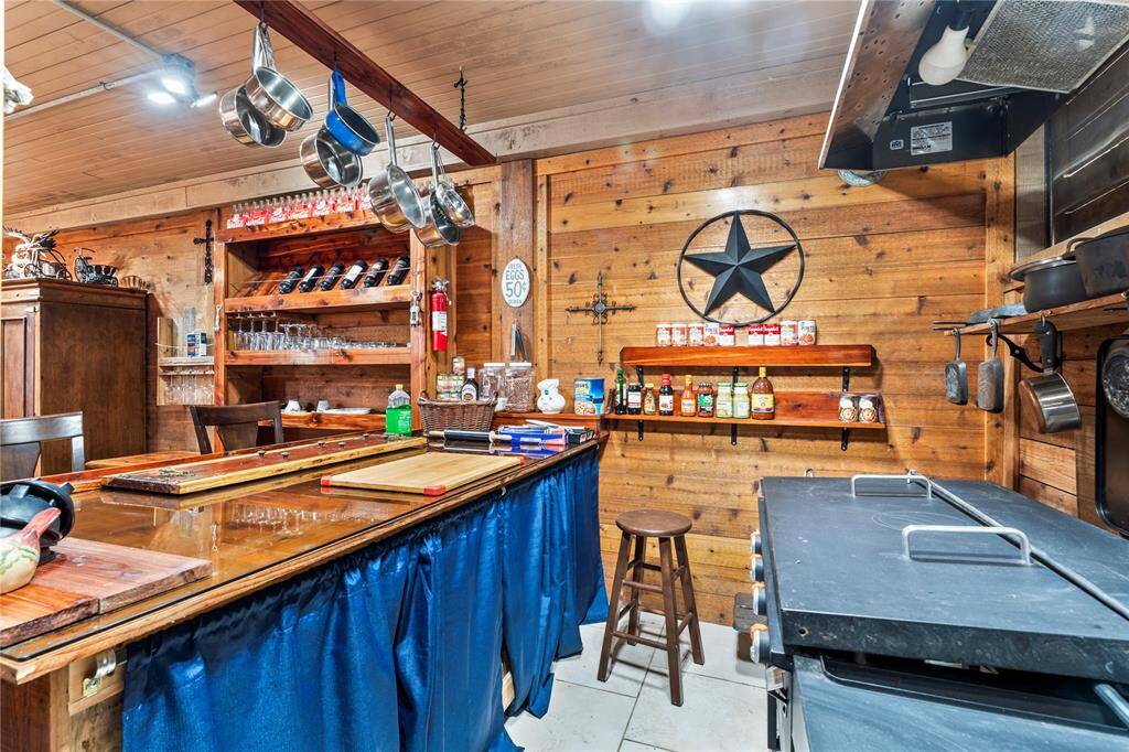 BBQ kitchen area has open shelving with ample storage, and a large cooking area. It includes a hanging pot rack and a charming bar counter, ideal for casual dining or entertaining.