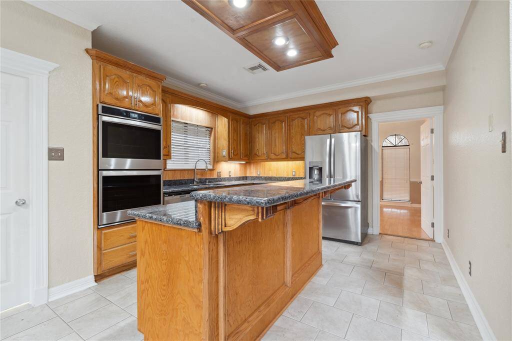 Granite countertops and stainless steel appliances, including a double oven and refrigerator. The central island offers additional prep space, and recessed lighting enhances the bright, inviting atmosphere.