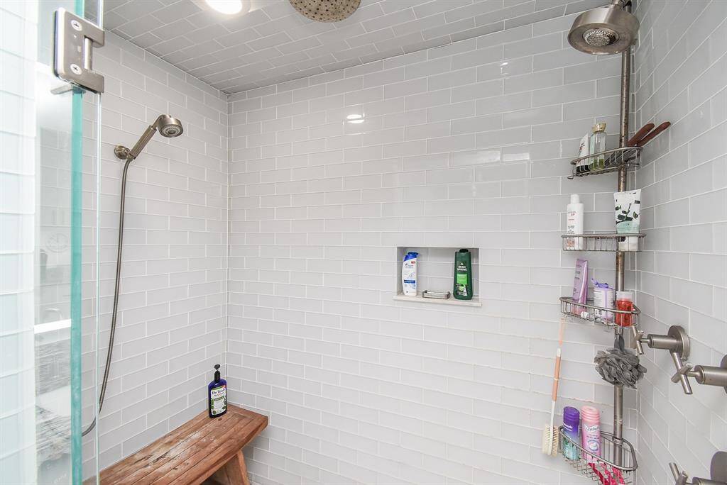 Spa-like shower with 3 different shower heads,  master temperature mixing valve, wood bench, shampoo niche and gorgeous light gray subway tile