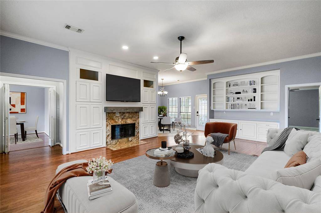 *Virtually Stage* Living room featuring ceiling fan, molding, a wood burning fireplace, built-in cabinets and hardwood floors. Updated texture and paint.