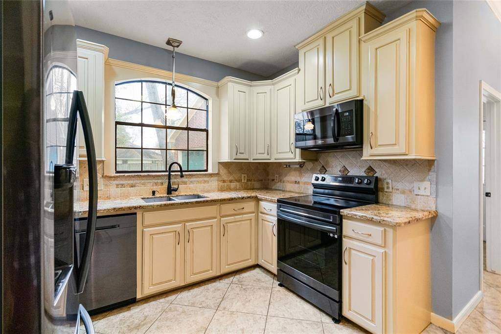 Kitchen featuring sink, tile backsplash, light stone granite counter tops, hanging light fixture, appliances