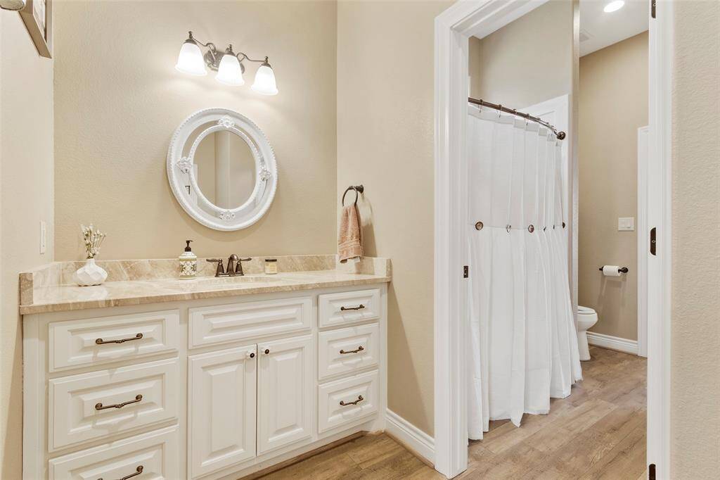 Jack n Jill bath bathroom between the secondary bedrooms. This bathroom features a classic design with a large vanity, granite counters, white cabinetry, and a round mirror.