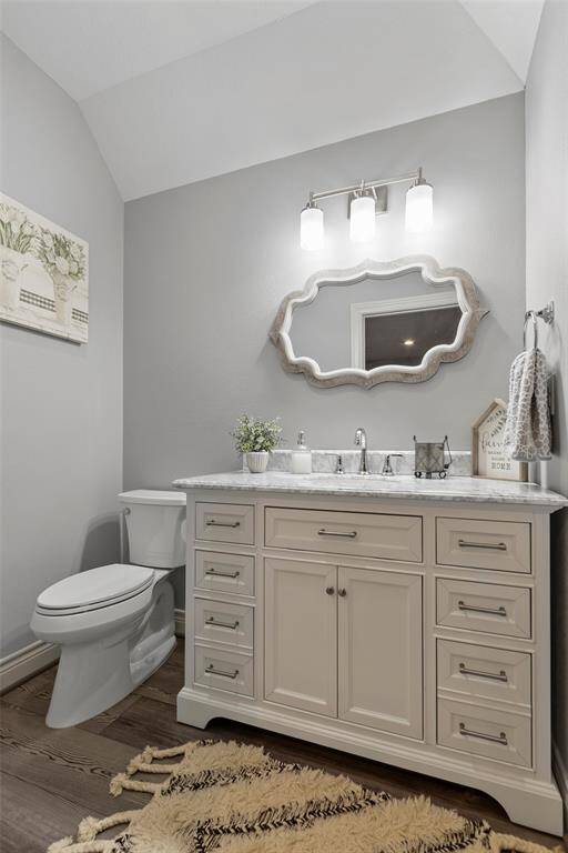 Convenient half bath off of the bunk room. This is a stylish powder room featuring a white vanity with ample storage, a unique mirror, and modern lighting. The walls are painted a soft gray, complemented by luxury vinyl flooring.