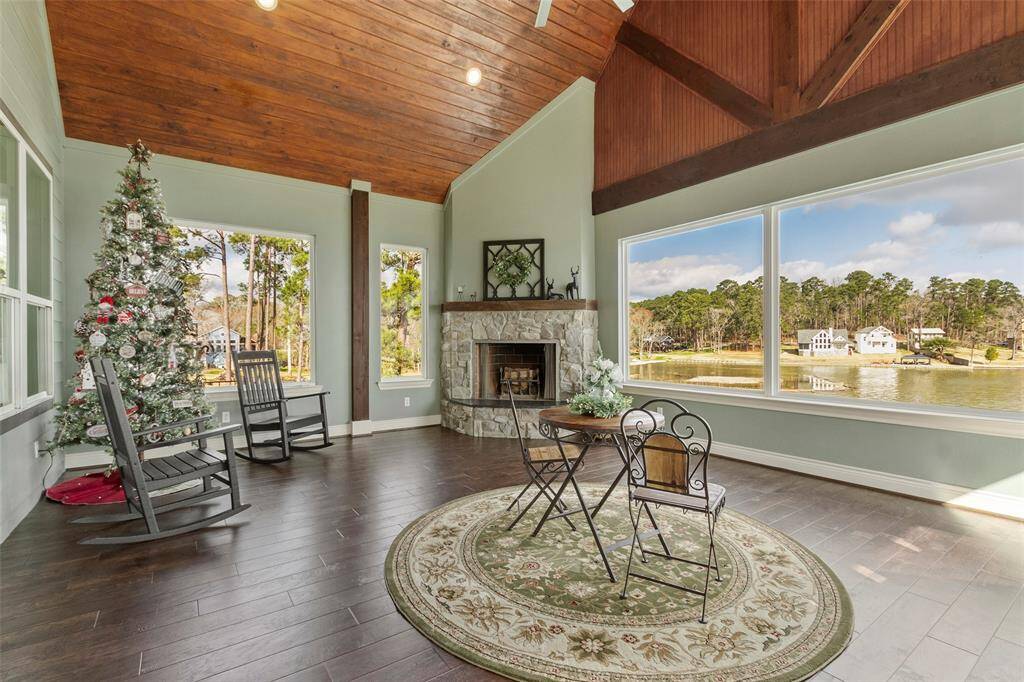 This photo showcases a bright, spacious sunroom with a wood-paneled ceiling and large windows offering panoramic lake views. It features a cozy stone fireplace creating a tranquil and inviting atmosphere.