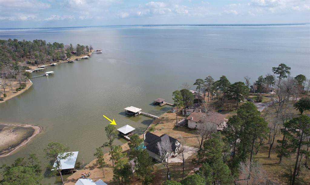 This aerial photo showcases a lakeside property nestled among trees, featuring a private dock extending into the water. The home offers scenic views and direct lake access, ideal for waterfront living. Nearby properties are similarly situated, creating a serene and picturesque neighborhood.