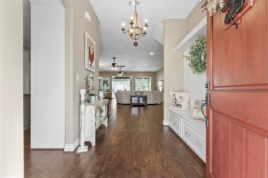 Welcome to a charming home with a warm entryway featuring hardwood floors and neutral walls. The hallway leads to a cozy living area with natural light and modern fixtures. A welcoming wooden front door and built-in bench add a touch of elegance. Perfect for comfortable, stylish living.