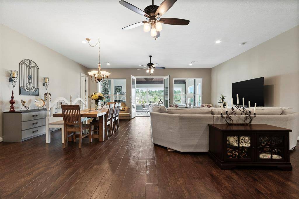 This spacious open-concept living and dining area features elegant hardwood floors, modern ceiling fans, and ample natural light from large glass doors leading to the sunroom. The room offers a cozy yet sophisticated atmosphere.