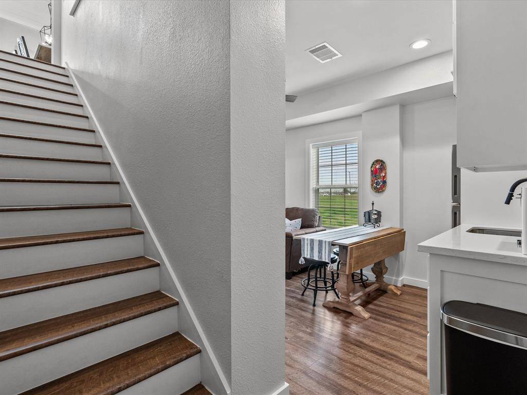 This photo features a modern, open-concept space with hardwood floors and a staircase leading to the upper level. The kitchen area includes a sleek countertop and a sink, while the adjacent dining area has a rustic wooden table and chairs, complemented by a window offering natural light.