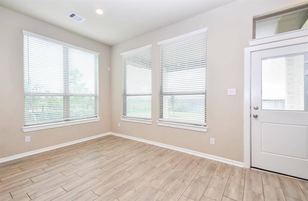 Bright breakfast room with light wood looking tile flooring, large windows with blinds, and a door leading outside.