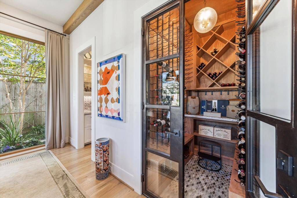 This photo showcases a stylish wine cellar with custom wooden racks and a glass door, adjacent to a bright room with a large window and elegant decor. Perfect for wine enthusiasts seeking a blend of functionality and design.