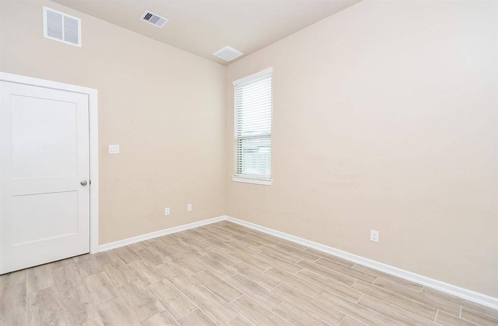 This second bedroom downstairs features neutral walls, wood-look tile flooring, and a window for natural light, creating a bright and versatile space.