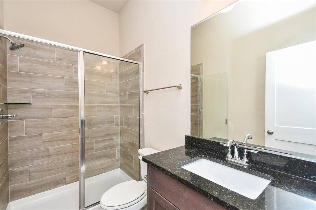 This full bathroom downstairs features a sleek modern design with a glass-enclosed shower, wood-look tile, and a dark granite countertop.