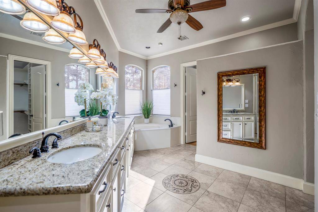 Light and bright en-suite offering dual sinks, tons of cabinetry, beautiful lighting, an overhead fan, a corner soaking tub, with beautiful arched windows above.