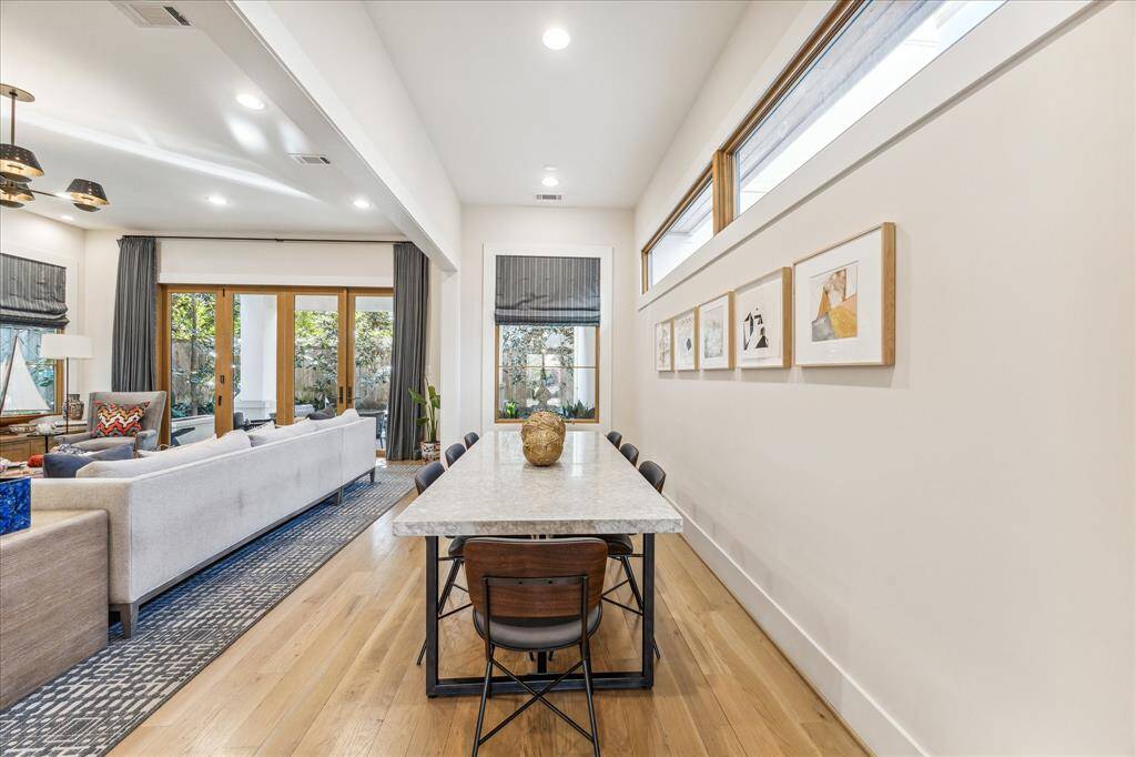This photo showcases a spacious and bright open-concept living and dining area with large windows, modern decor, and a seamless flow. The room features light wood flooring, a long dining table, and ample seating, creating an inviting and functional space for entertaining.