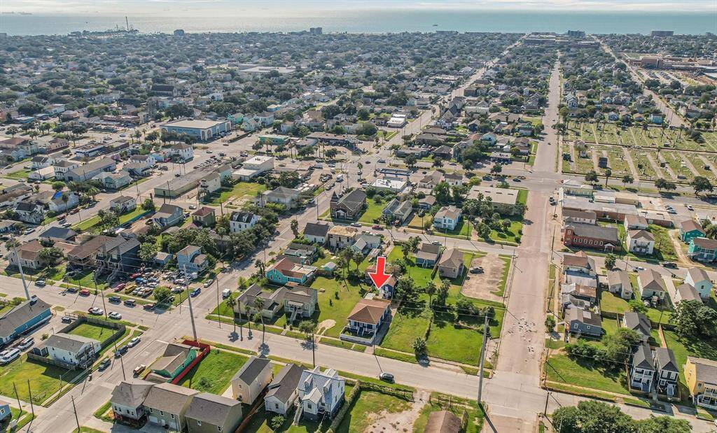 This aerial photo showcases a residential neighborhood near the coast, highlighting a specific property with a red arrow. The area features a mix of homes, greenery, and proximity to the water, offering a blend of urban and suburban living.