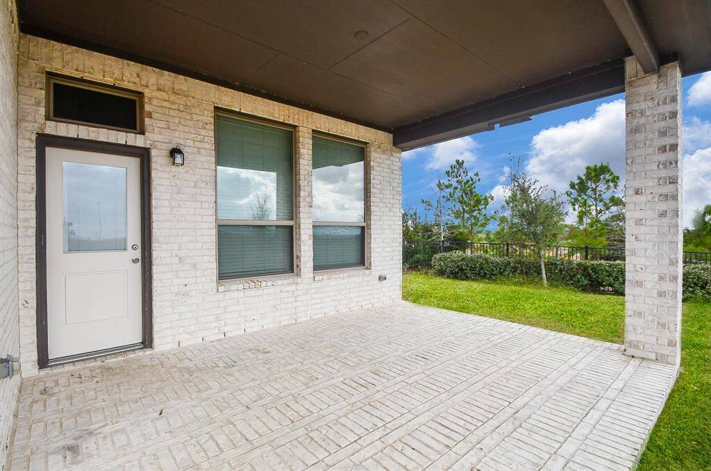 This photo showcases a covered patio with a charming white brick exterior, offering a spacious outdoor retreat. Overlooking a lush grassy yard and serene trees, this inviting space is perfect for relaxing or entertaining in any season.