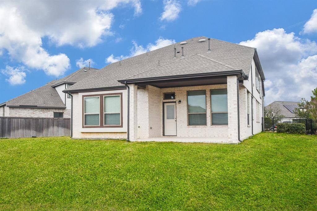 This photo shows a modern two-story home with a spacious backyard. The exterior features light brick and a covered patio area, ideal for outdoor relaxation. The property is fenced, providing privacy and security.