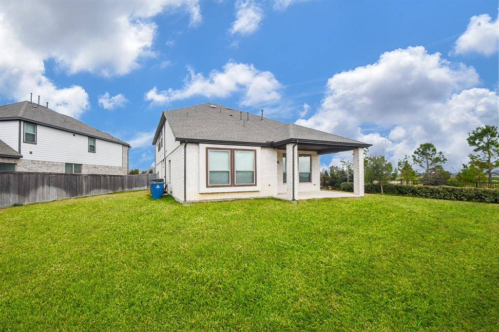 This photo shows a modern, single-story home with a spacious backyard. It features a covered patio area, a well-maintained lawn, and is situated in a quiet neighborhood with a neighboring house nearby.