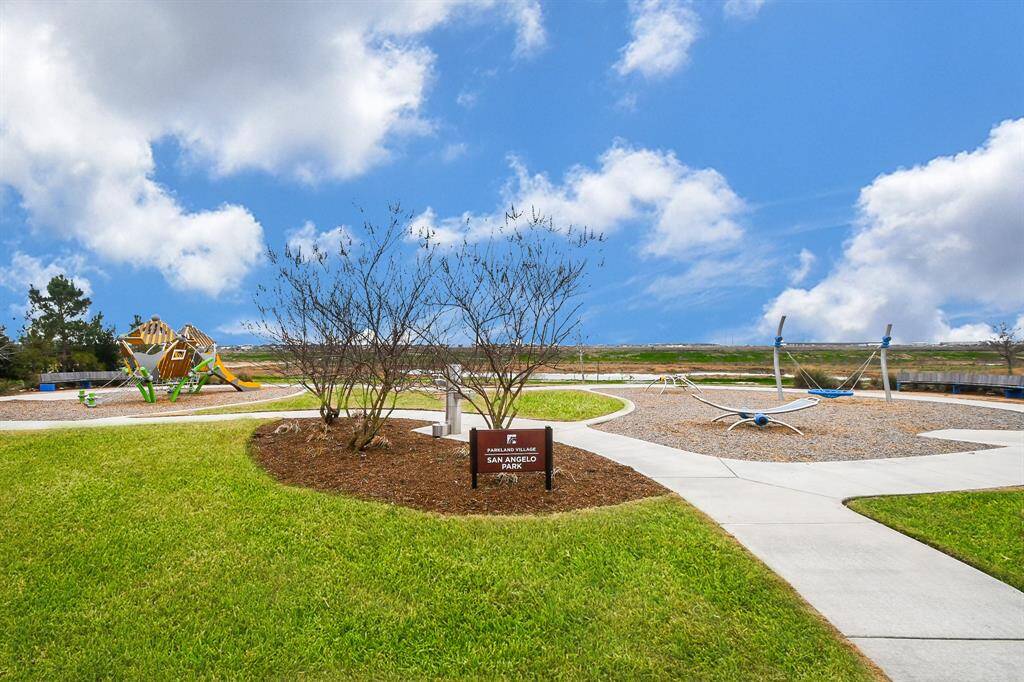 This photo showcases a well-maintained community park with a modern playground and open green spaces, perfect for families and outdoor activities. The clear blue sky adds to the inviting atmosphere.