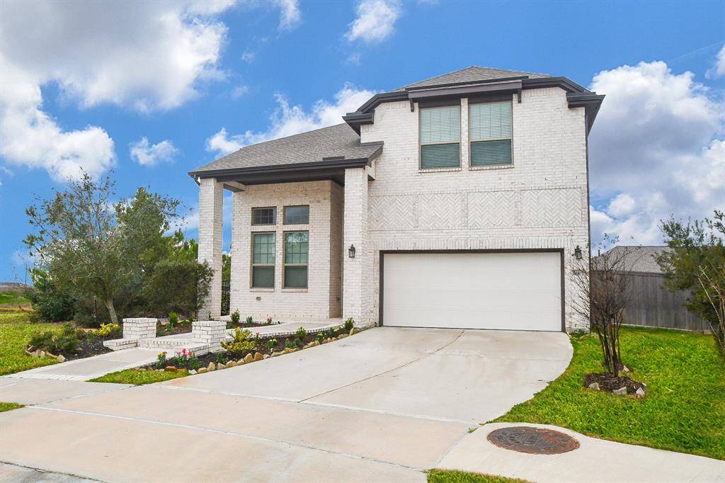 This photo showcases a modern, two-story white brick home with a two-car garage and a well-maintained front yard. The driveway is spacious, and the house features large windows and a neatly landscaped entrance. Perfect for buyers seeking a contemporary look.