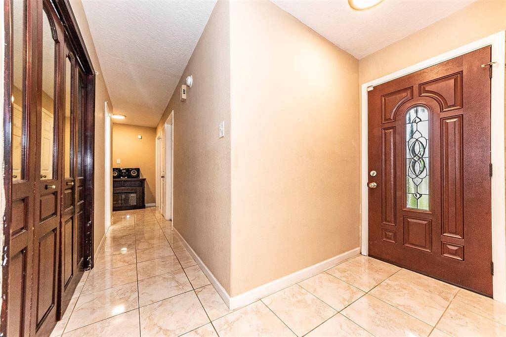 This photo shows a bright, well-lit hallway featuring a polished tiled floor. It includes an elegant wooden front door with decorative glass and leads to multiple rooms, offering a warm and inviting entryway.