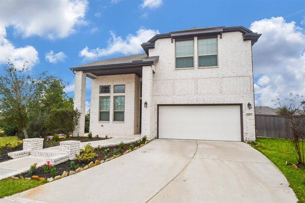 This modern two-story home features a clean white brick exterior, a spacious two-car garage, and a well-maintained front yard with attractive landscaping. It offers a welcoming entrance with large windows, adding to its bright and airy feel.