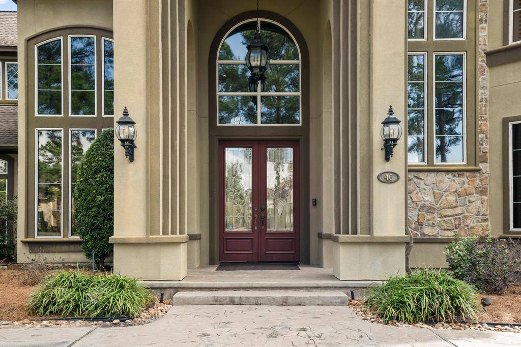Impressive double mahogany and lead glass doors, framed by a tall, arched entryway with gorgeous coach lights flanked on either side, these elegant features contribute to the estate's overall grandeur and welcoming atmosphere.