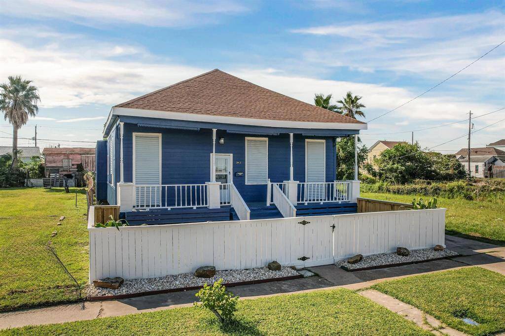 This charming single-story home features a blue exterior with a cozy front porch and white railing. It is surrounded by a well-maintained lawn and enclosed by a decorative white fence. The property offers a spacious yard, perfect for outdoor activities.