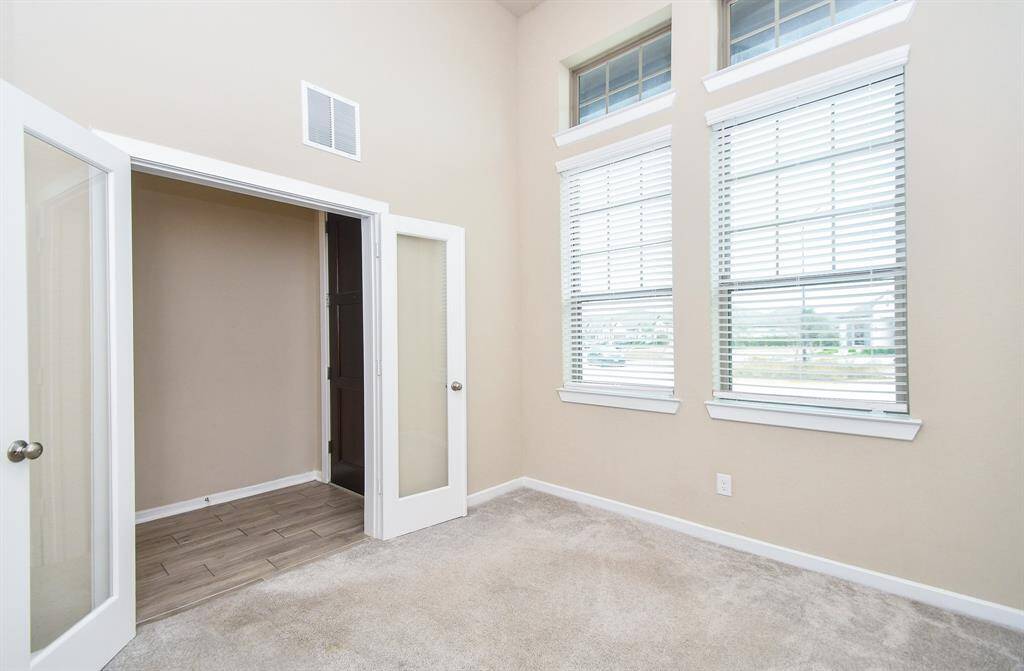 A sophisticated study room featuring elegant French doors that open to a bright and inviting space. The soaring high ceiling enhances the sense of openness, while large windows allow natural light to flood the room, creating an inspiring atmosphere. Perfect for work or study, this space offers both privacy and style, making it an ideal home office or reading retreat