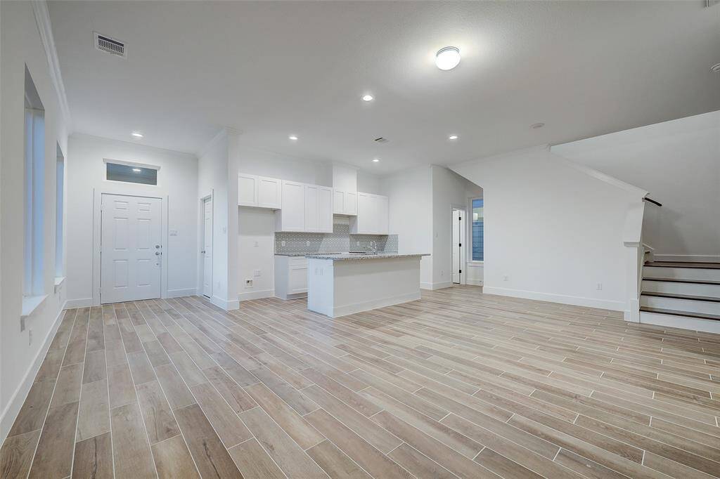 View of the home's entrance and expansive living quarters. Wood-like tile flooring is offered throughout the 1st floor. Large windows allow the easy flow of natural light and are complemented by recessed lighting throughout the space.