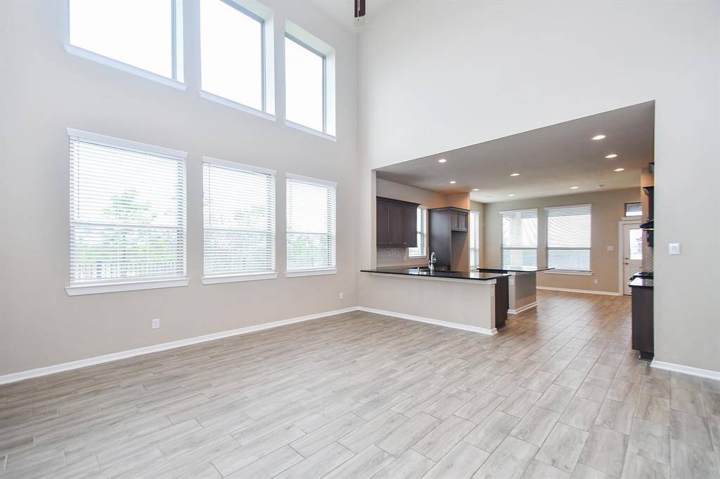 This photo highlights a spacious, open-concept living area with soaring ceilings and an abundance of natural light. The modern kitchen boasts sleek cabinetry and a large island, seamlessly integrating with the dining and living spaces. Light wood like tile flooring enhances the bright, airy ambiance, creating a perfect blend of style and functionality.