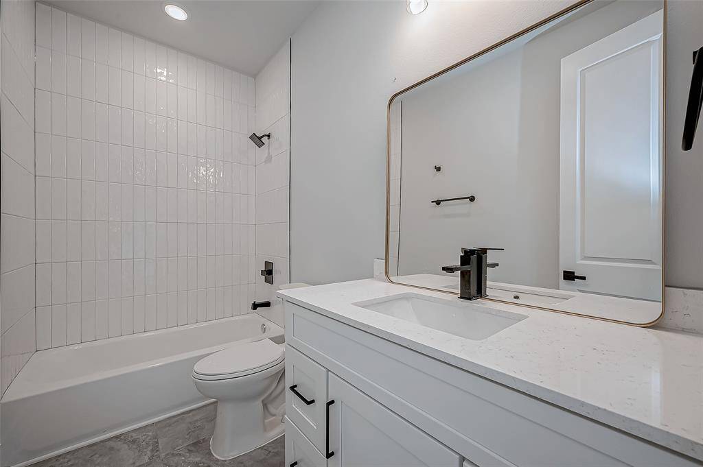 This photo shows a bright laundry room with hookups for a washer and dryer, featuring white walls, a window for natural light, and black hexagonal tile flooring. There are two wooden shelves for storage.