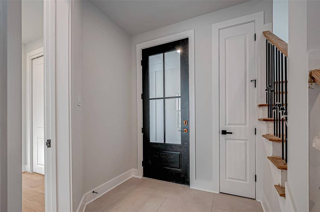 A spacious, open-concept living area with hardwood floors, abundant natural light, and a modern kitchen featuring white cabinetry and a central island. The room includes recessed lighting, a ceiling fan, and access to a balcony through large double doors, offering a bright and inviting atmosphere.