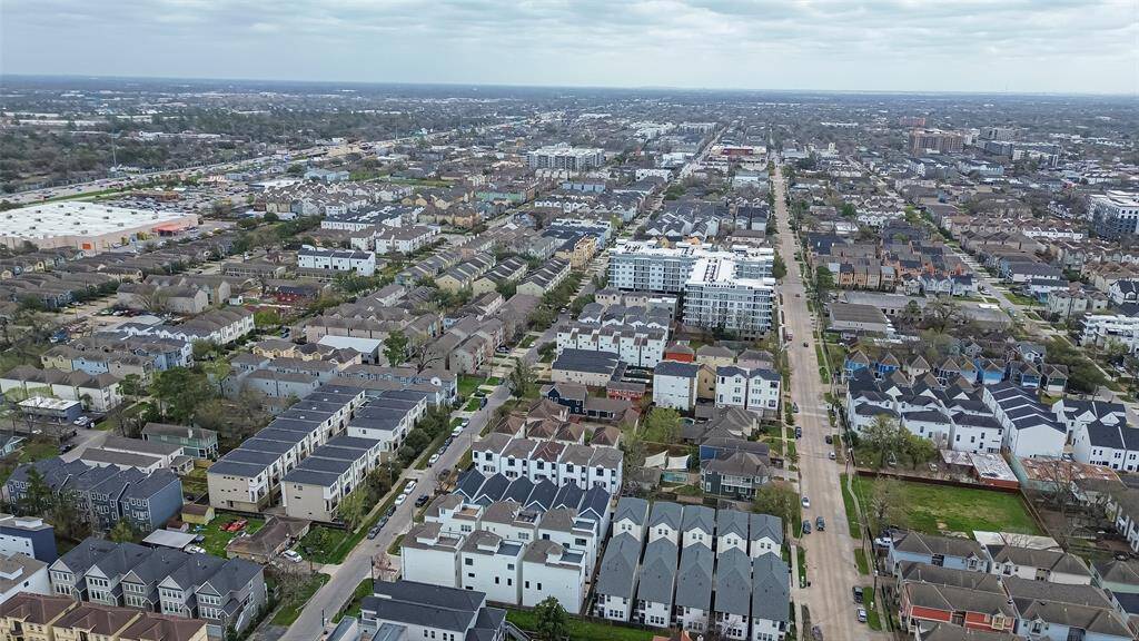 This aerial photo showcases a modern townhouse in a densely populated neighborhood. The home is highlighted with a red arrow, indicating its location within a cluster of similar homes. The area appears vibrant and urban, with a city skyline visible in the distance, suggesting proximity to downtown amenities.