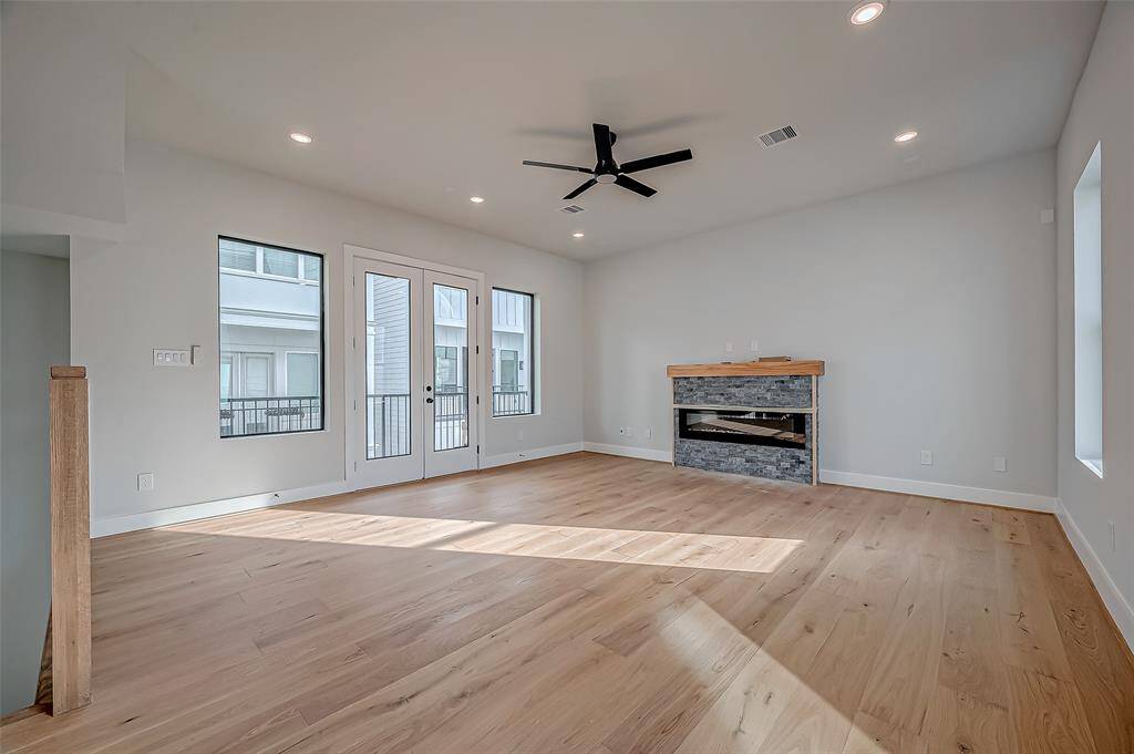 This is a bright, modern bedroom on the first floor with light wood flooring and neutral walls. It features a ceiling fan, a spacious closet with sliding doors, and an en-suite bathroom. The room has recessed lighting and an open doorway leading to a staircase.