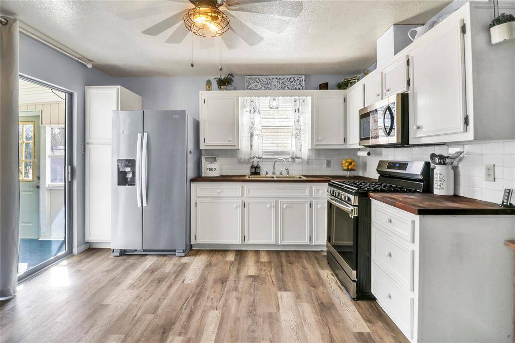 This kitchen features white cabinetry with butcher block countertops, a ceiling fan, and a window above the sink for natural light. The space opens to a screened porch, creating an inviting and functional layout.