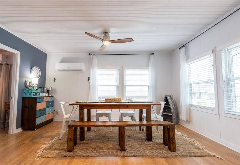 This dining area features a cozy, rustic design with a wooden table and benches, complemented by a textured rug. Large windows allow ample natural light, and the room is accented by a colorful coffee bar and a modern ceiling fan.  Seating for 8.